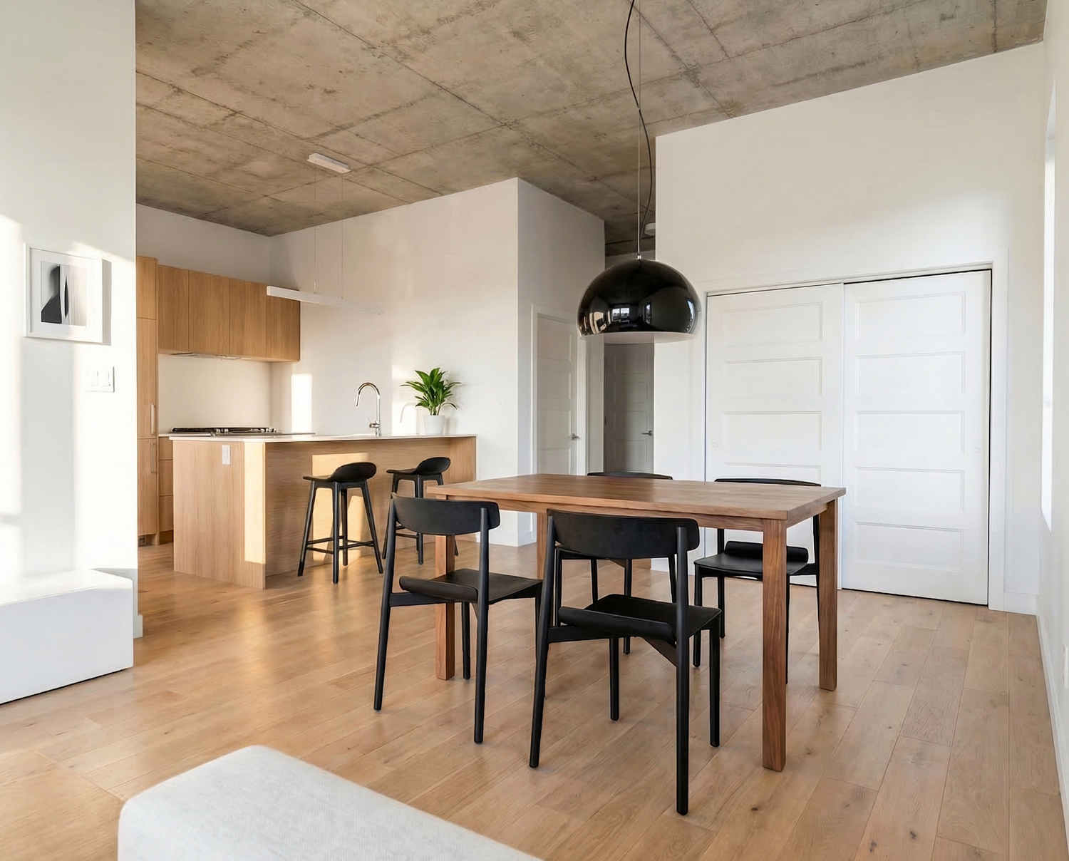 Salle à manger moderne avec table en bois, chaises noires et lustre noir sur plafond en béton.